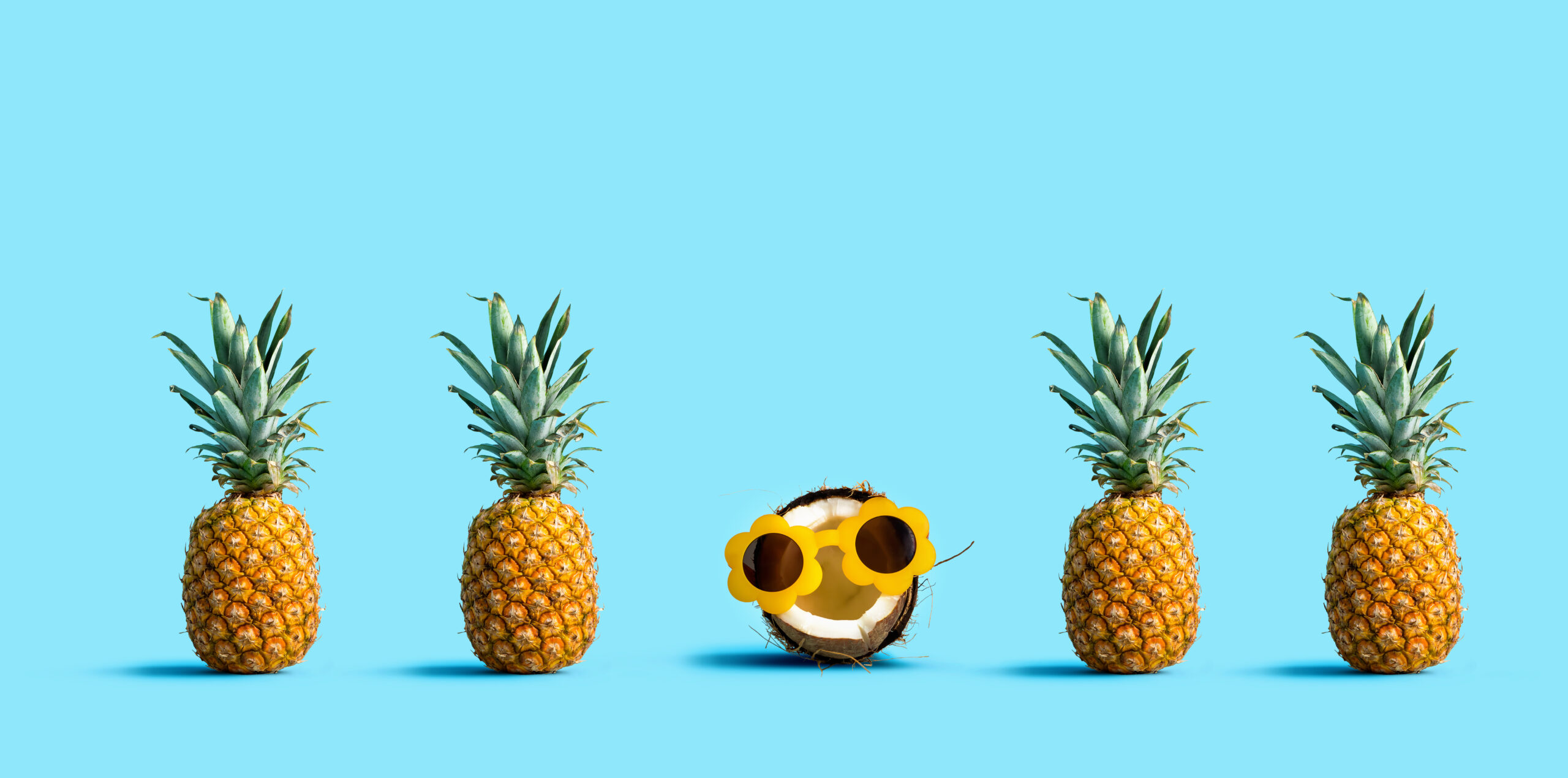 One out unique coconut wearing sunglasses with many pineapples